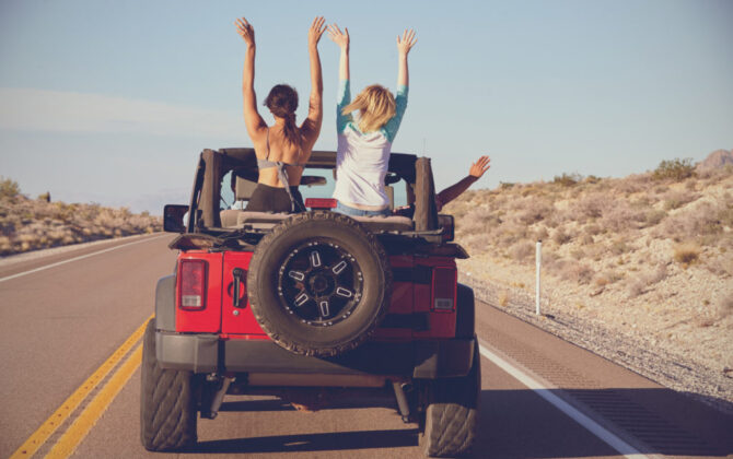 A jeep driving with two girls sitting in the backseat.