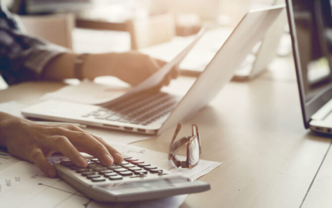 A young man making his budget using his calculator and laptop.