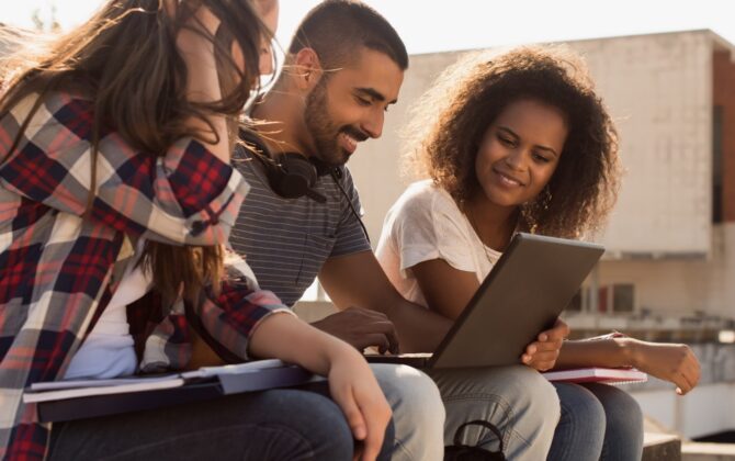 Three students sitting outside and look at one's laptop, understand the different types of student loan repayment options.