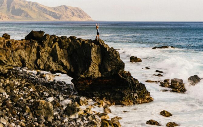 a young man standing over rocks near beach