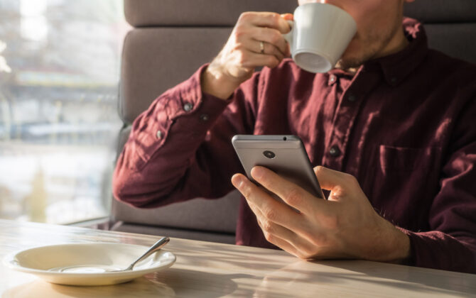 A young man drinking coffee and researching on a mobile phone