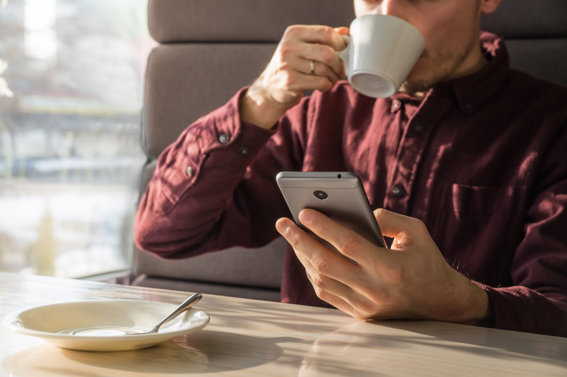 A young man drinking coffee and researching on a mobile phone