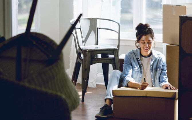 young woman sitting on the floor with boxes, writing things to do first for her new home