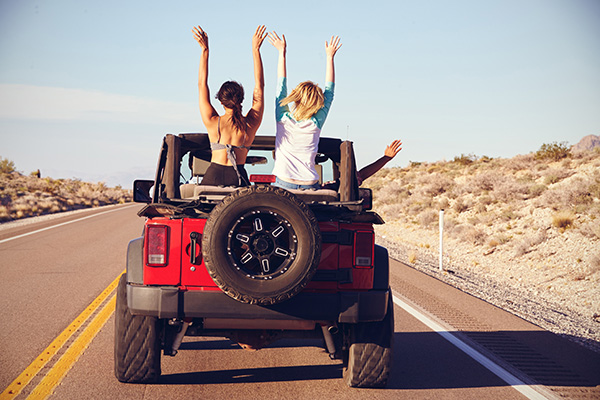 A jeep driving with two girls sitting in the backseat.