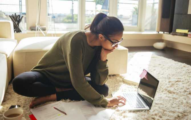 Young woman sitting on the floor studying and working on the laptop