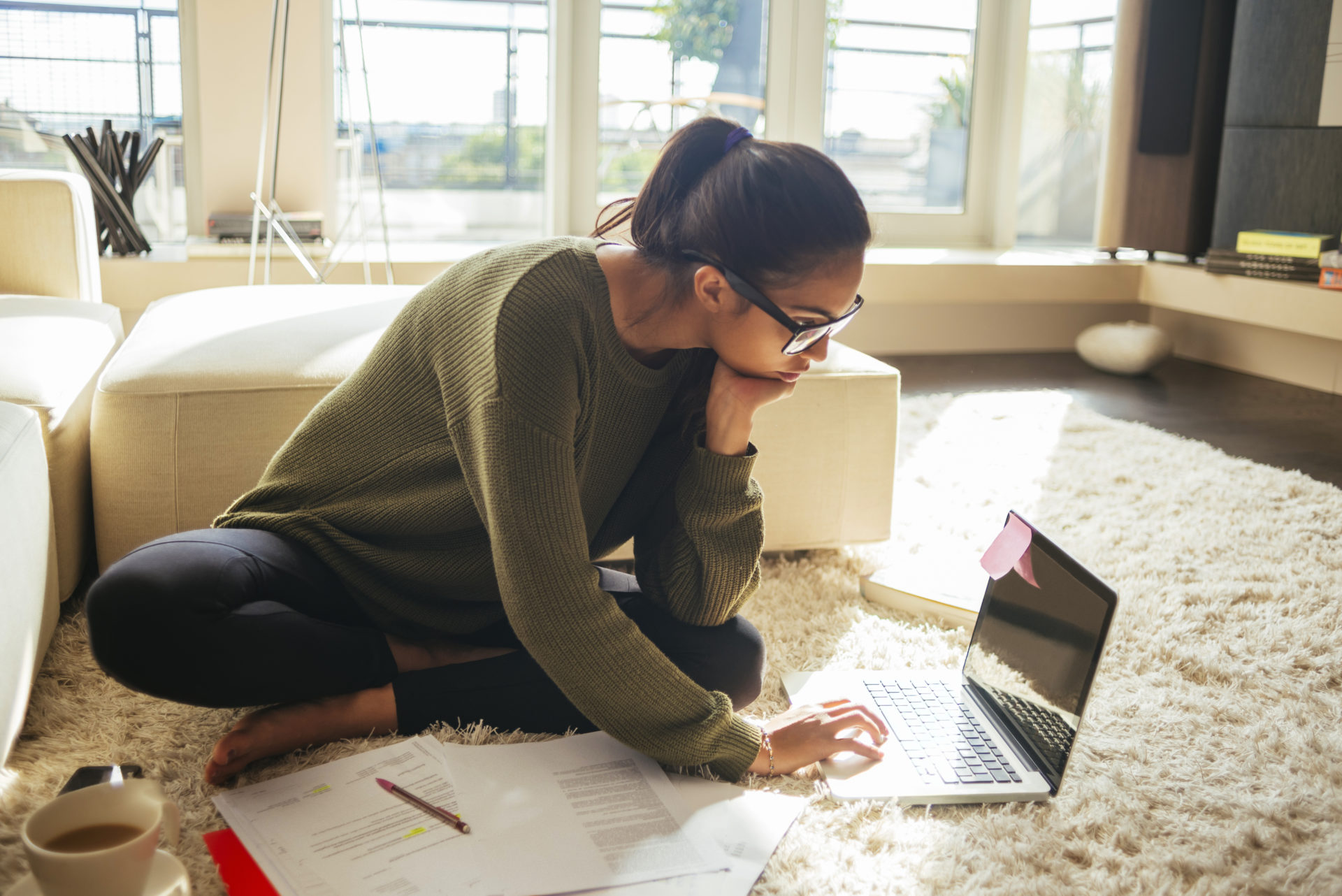 Young woman sitting on the floor studying and working on the laptop