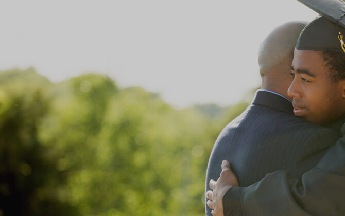 A graduate student wearing convocation ropb and hugging his father.