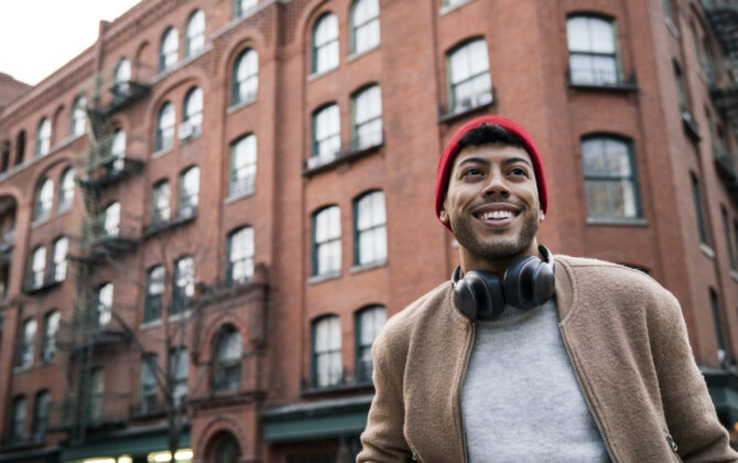 Young man standing on city street smiling, happy about the federal student loan repayment programs.