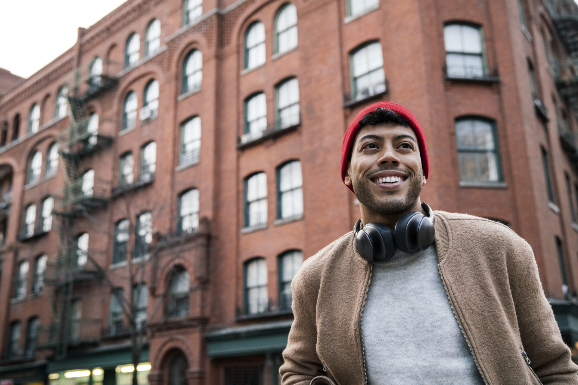 Young man standing on city street smiling, happy about the federal student loan repayment programs.