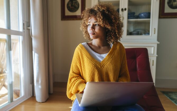 A young woman sitting on chaiselongue reading about student loan refinance rates and terms.