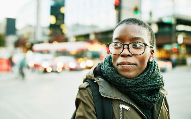 College student with glasses walking through the city, thinking about how to pay off student loan.