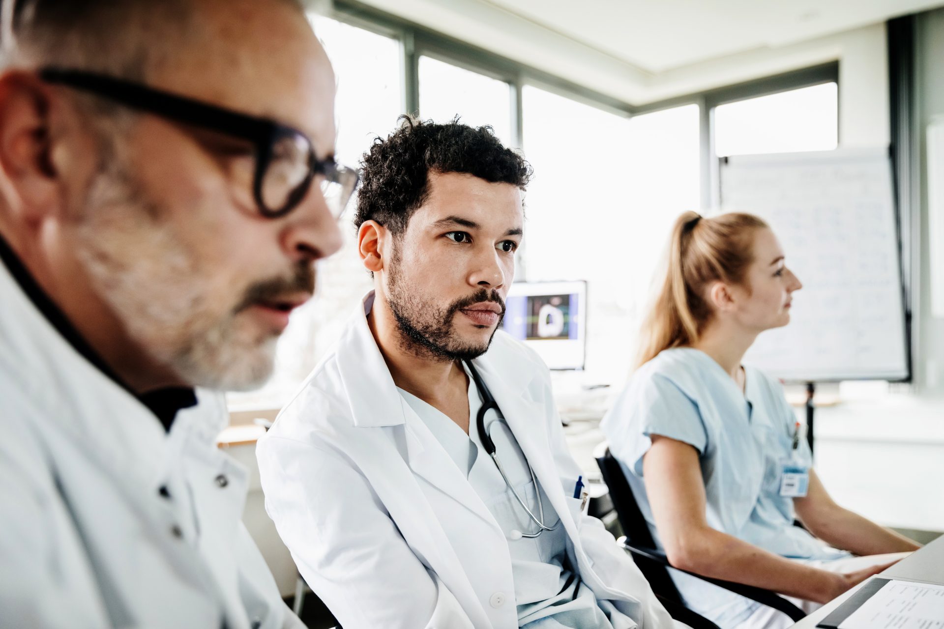 A medical student with a white coat sitting in a classroom with a teacher beside him.