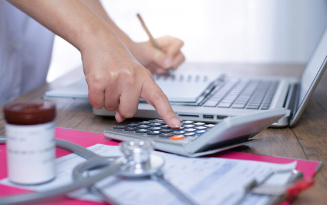 doctor creating a financial plan with a calculator, notebook, and computer