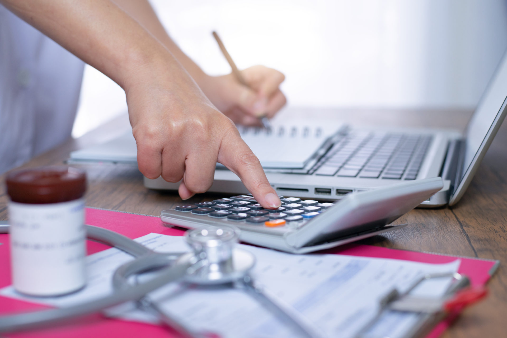 Doctor creating a financial plan with a calculator, notebook, and computer.