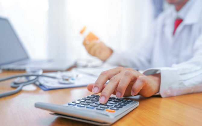 A doctor creating a budget by using a calculator and notebook.