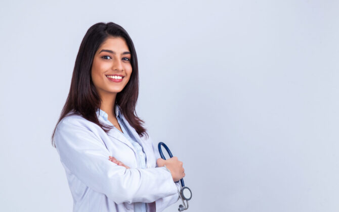 Indian female doctor in white coat with stethoscope, waist up.