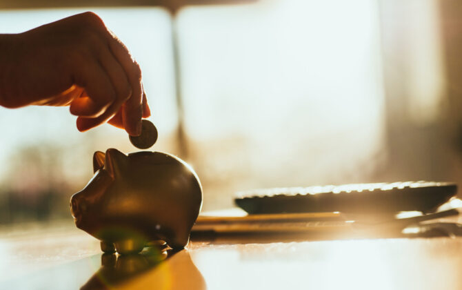 A hand putting a coin in a gold colored piggy bank at home.