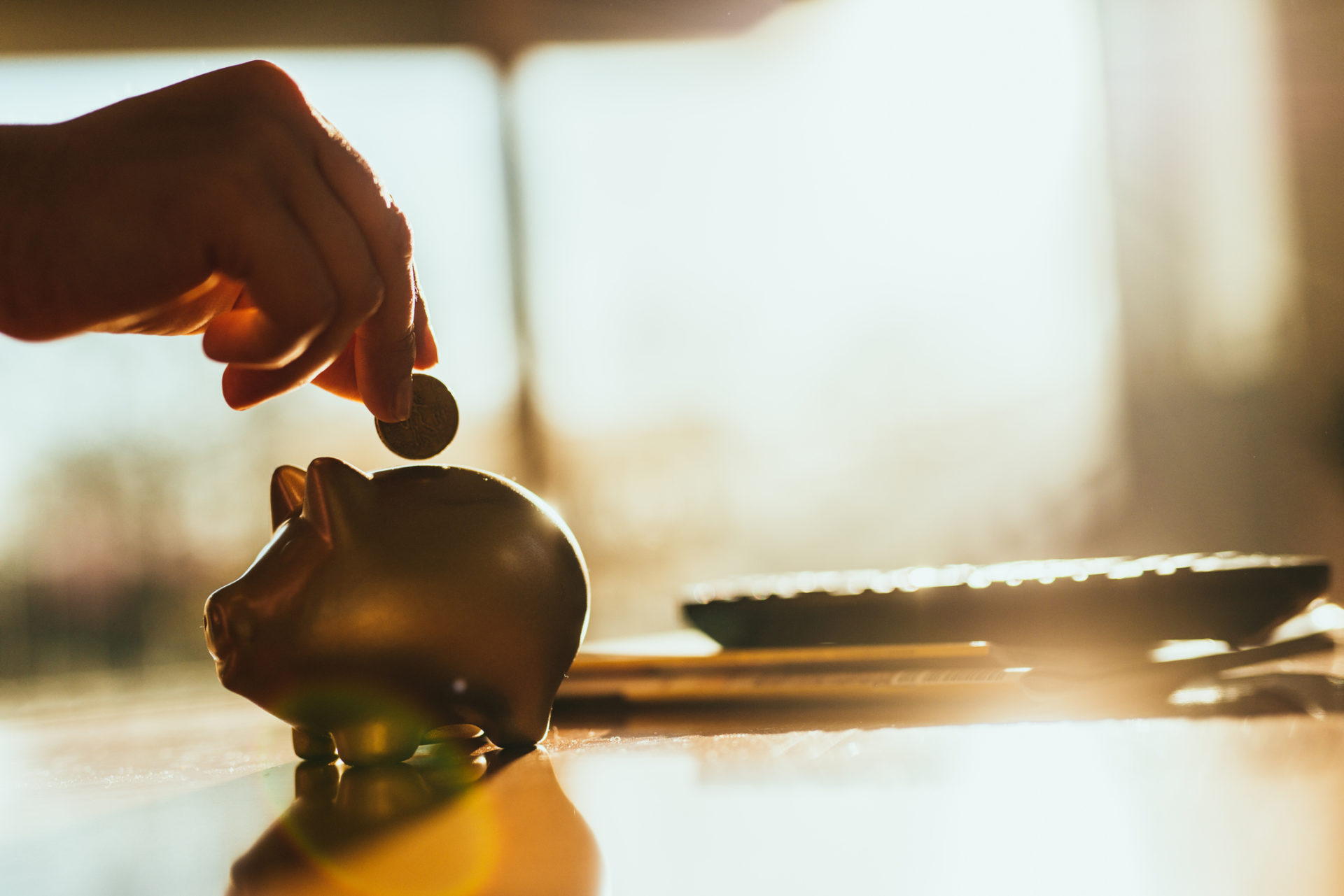 A hand putting a coin in a gold colored piggy bank at home.