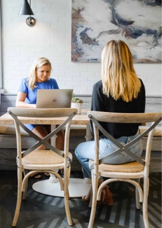 Two women at cafe table, working on laptops.