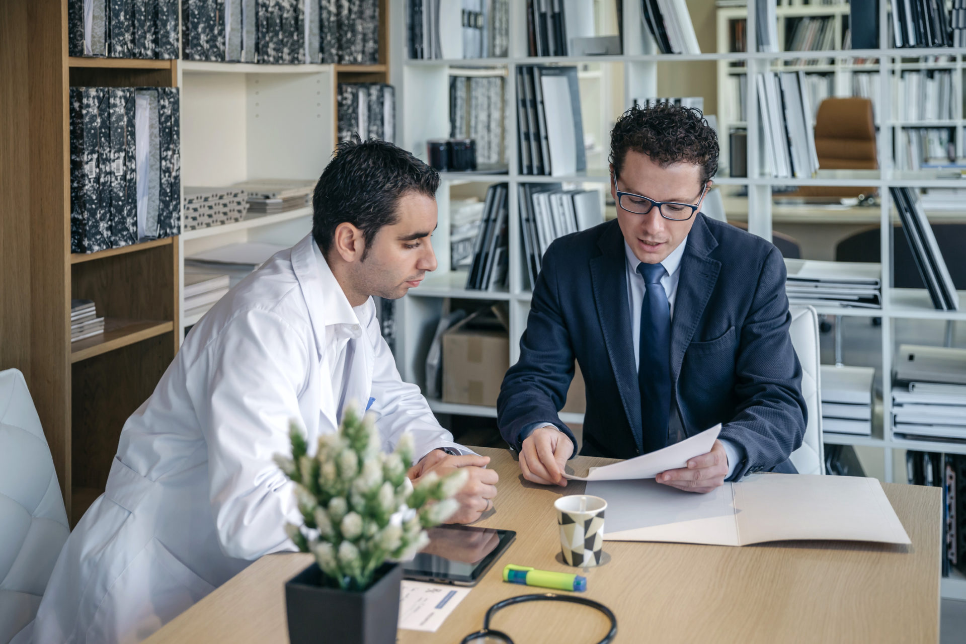 Man in suit explaining documents to doctor in medical office.