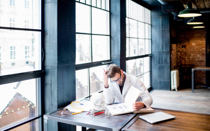 a male doctor wearing white coat with laptop and books on the table, and creating a study plan