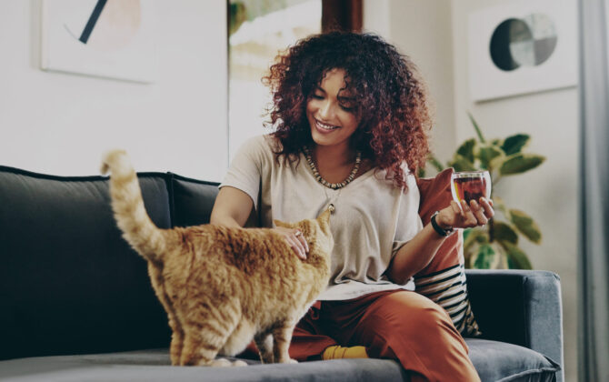 Shot of an attractive young woman drinking tea while relaxing with her cat at home