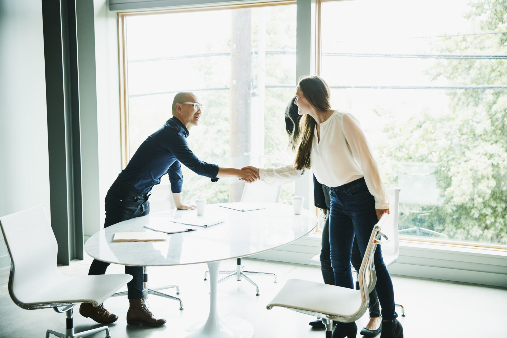 Businesswoman shaking hands with client before meeting in office conference room.