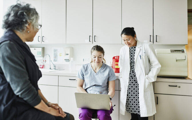 Female doctor and nurse reviewing patients chart on laptop during appointment in exam room