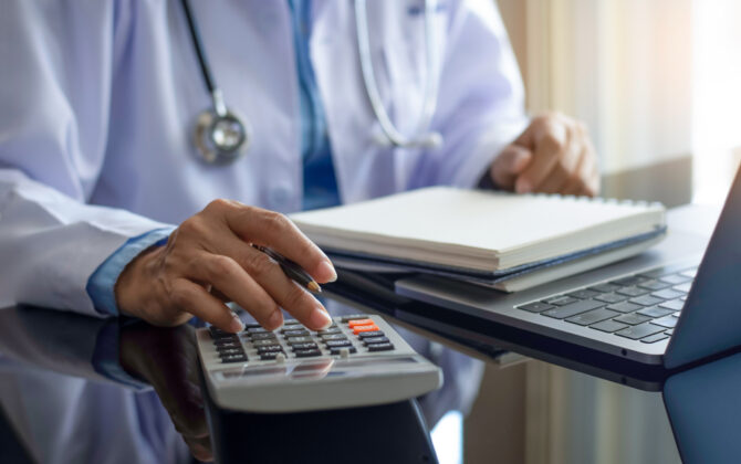 A doctor creating an investment plan by using a calculator and a laptop