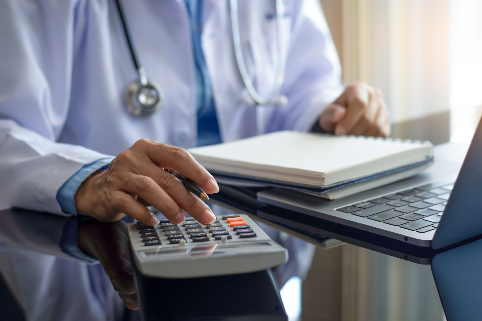 A doctor creating an investment plan by using a calculator and a laptop