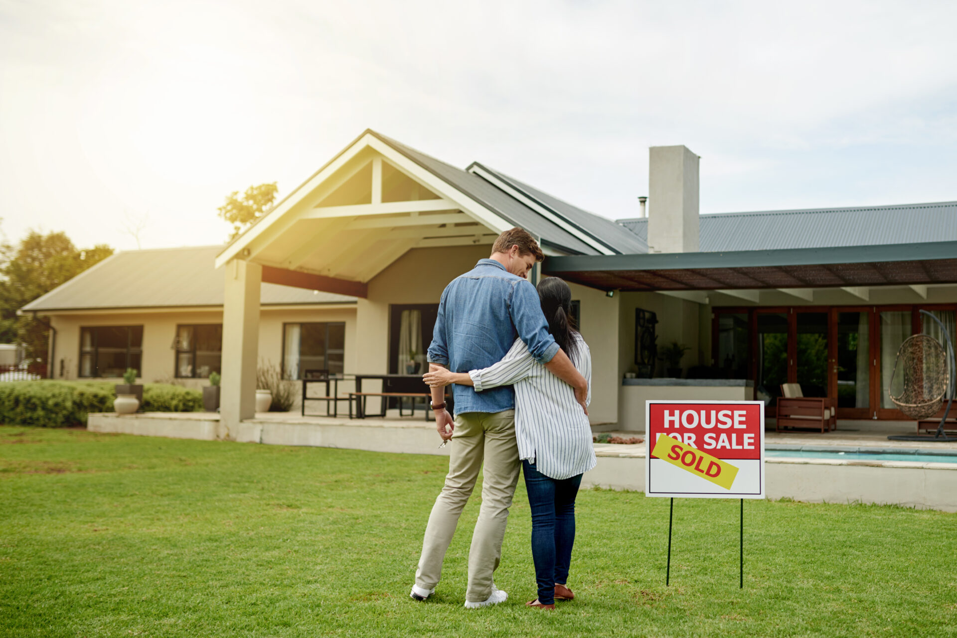 Shot of a couple standing next to a real estate sold sign at their new house