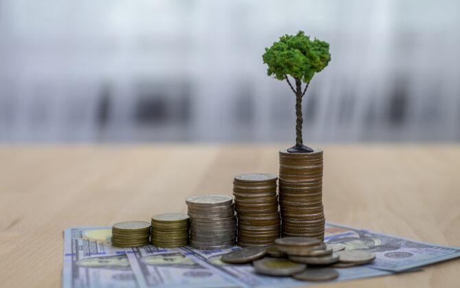 Progressively larger stacks of coins on hundred dollar bills, with a small tree to illustrate growth of savings.