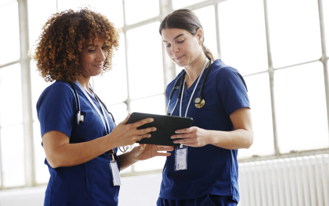 Two healthcare professionals in conversation, looking at digital tablet