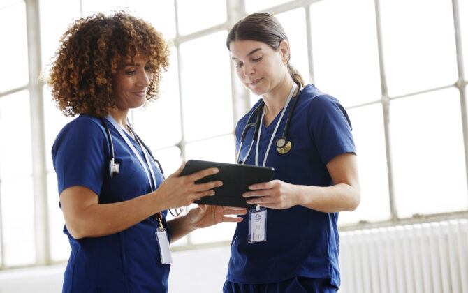 Two nurses in conversation, looking at digital tablet