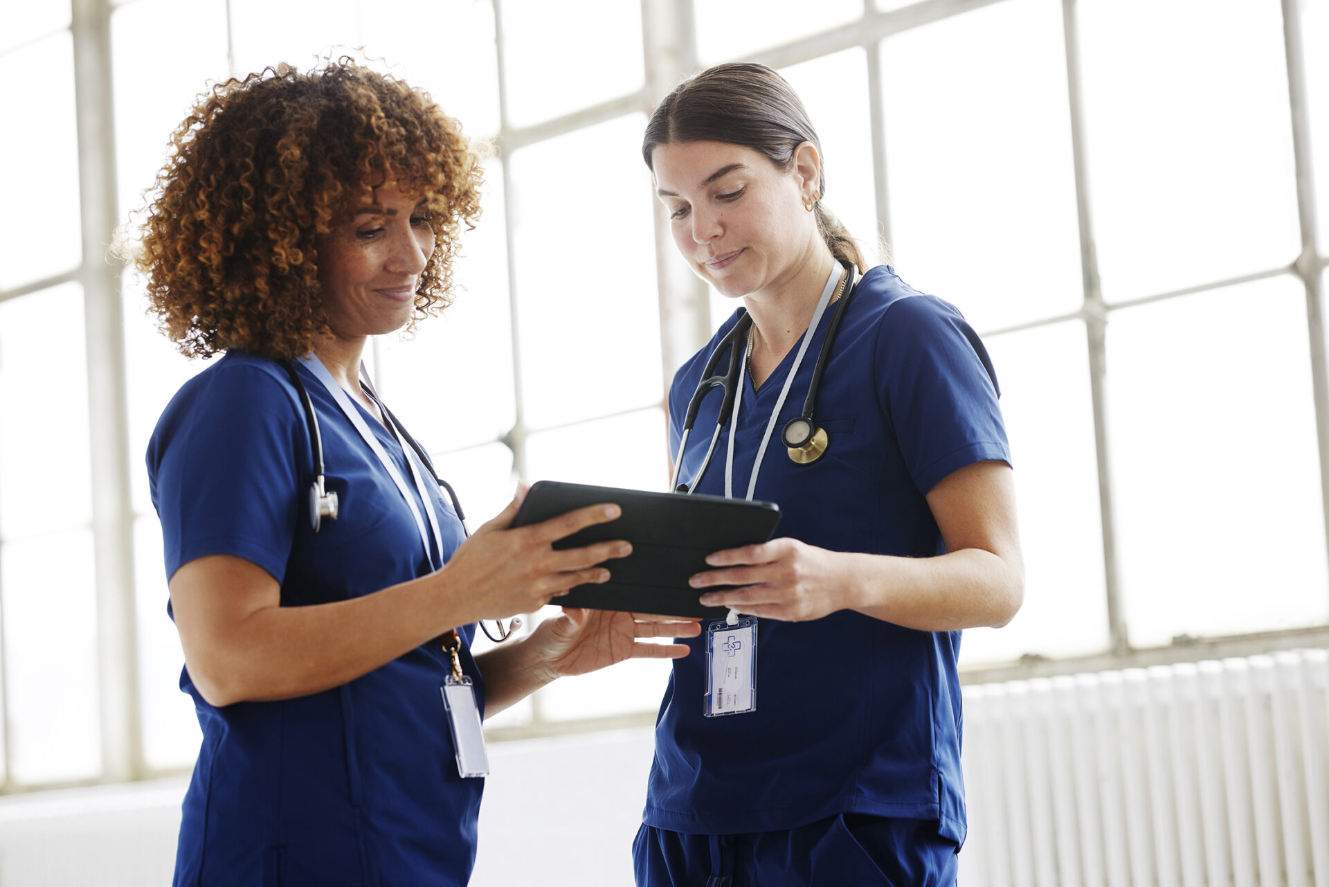 Two nurses in conversation, looking at digital tablet