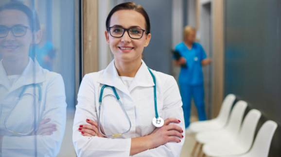 Middle aged white female physician in white coat, smiling, arms crossed, in a hospital.