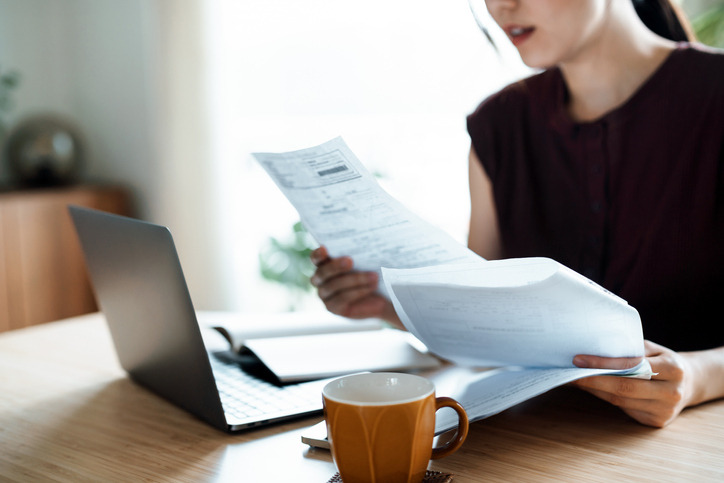 Cropped shot of Asian woman sitting at dining table, handling personal finance with laptop. She is making financial plan and planning budget as she go through her financial bills, tax and expenses at home. Wealth management, banking and finance concept