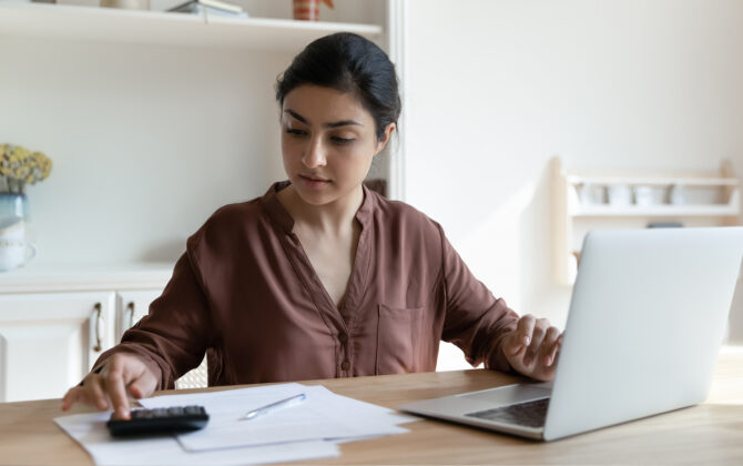 Focused young Indian woman sitting at a table and calculates income-driven repayment